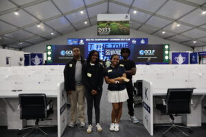 Four individuals pose together in a large indoor space, likely a sports event venue, with a digital display in the background.