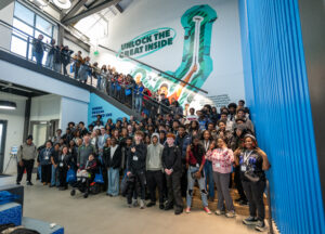 A large group of people poses together in a modern building with a mural that reads "Unlock the Great Inside."
